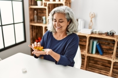  Middle age grey-haired woman taking pills sitting on the table at home.