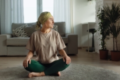 Young woman with cancer taking yoga and meditating in her apartment.