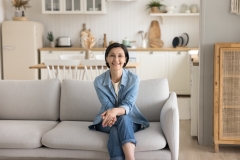 Attractive middle-aged woman housewife in casual clothes relaxing sit on sofa at home, smile look at camera feel satisfied with calm, well-being retired life. Portrait of happy homeowner or tenant