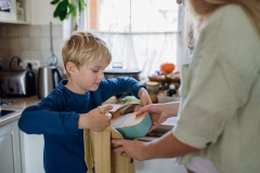 Mom packing snack for her son for school. Putting lunch box with healthy snack into his school bag for lunch.