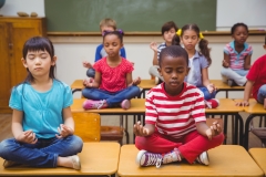 Pupils meditating in lotus position on desk in classroom at the elementary school