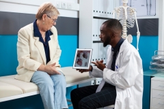 Elderly caucasian woman listens as black male physician goes over treatment details on tablet. African american doctor using digital device to explain heart diagnosis to senior female patient.