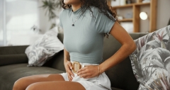 Woman, hands and stomach pain in home, period and abdomen inflammation for uterus risk in lounge. Endometriosis, menstrual cycle and pcos for chronic disease, constipation and indigestion issues