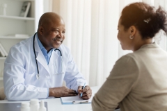 Smiling Black Doctor In Uniform Consulting Female Patient During Meeting In Clinic