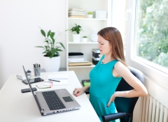 Image of a young woman having a back pain while sitting at the working desk