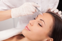 Close up of hands of expert beautician injecting botox in female forehead.