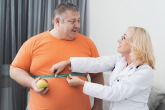 Obese Man with Doctor in White Coat in Gray Room.